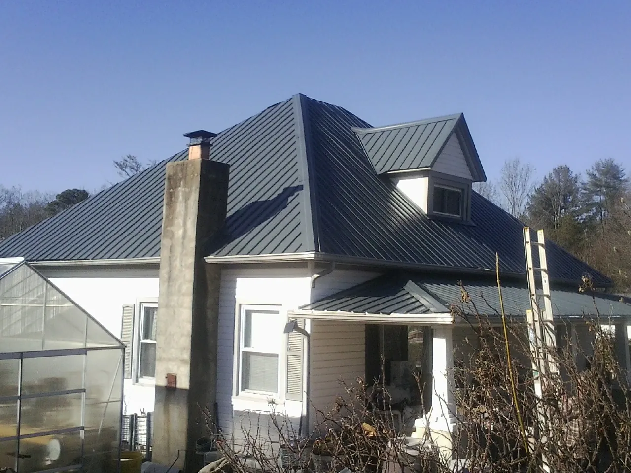 Dark blue standing seam metal roof on a white farmhouse with dormer — Slate & Tile Roof Repair by Roofing Brothers in Flora