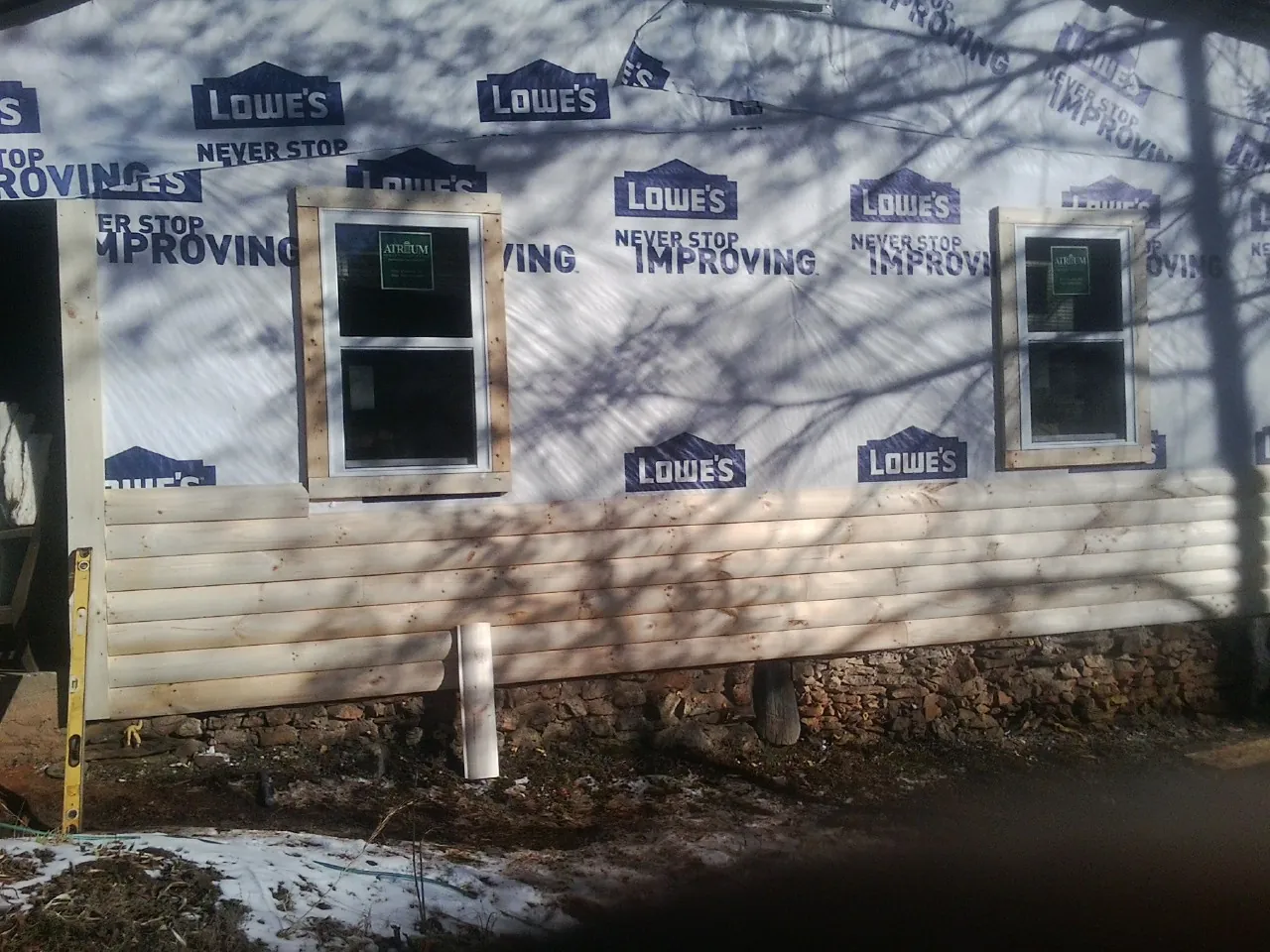 House wrap and new log siding going up on an exterior wall in Flora