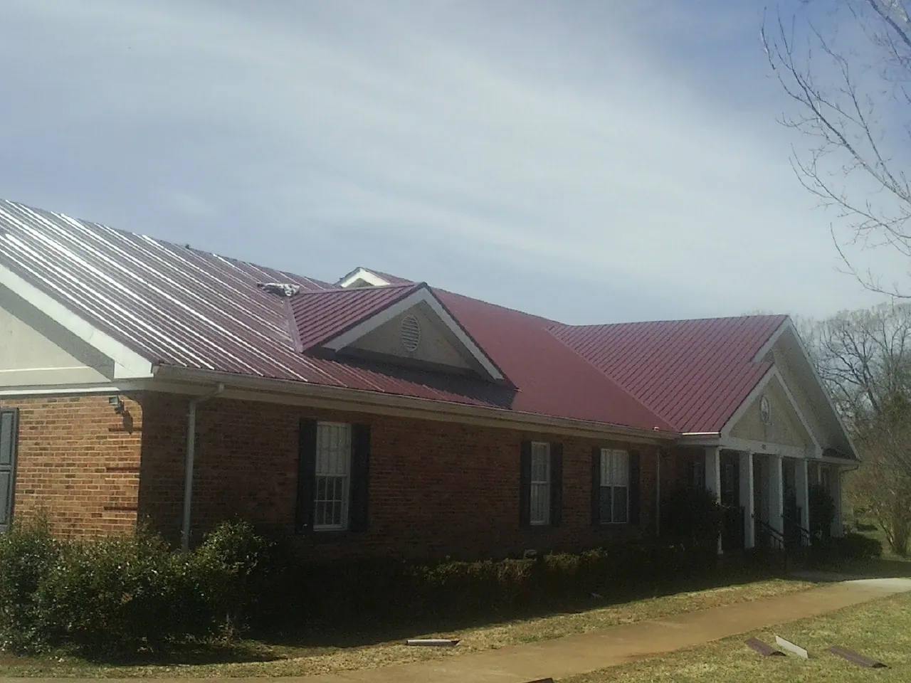 Red metal roof with gabled entries on a long brick building, from a Hail Damage Roof Repair job in Flora