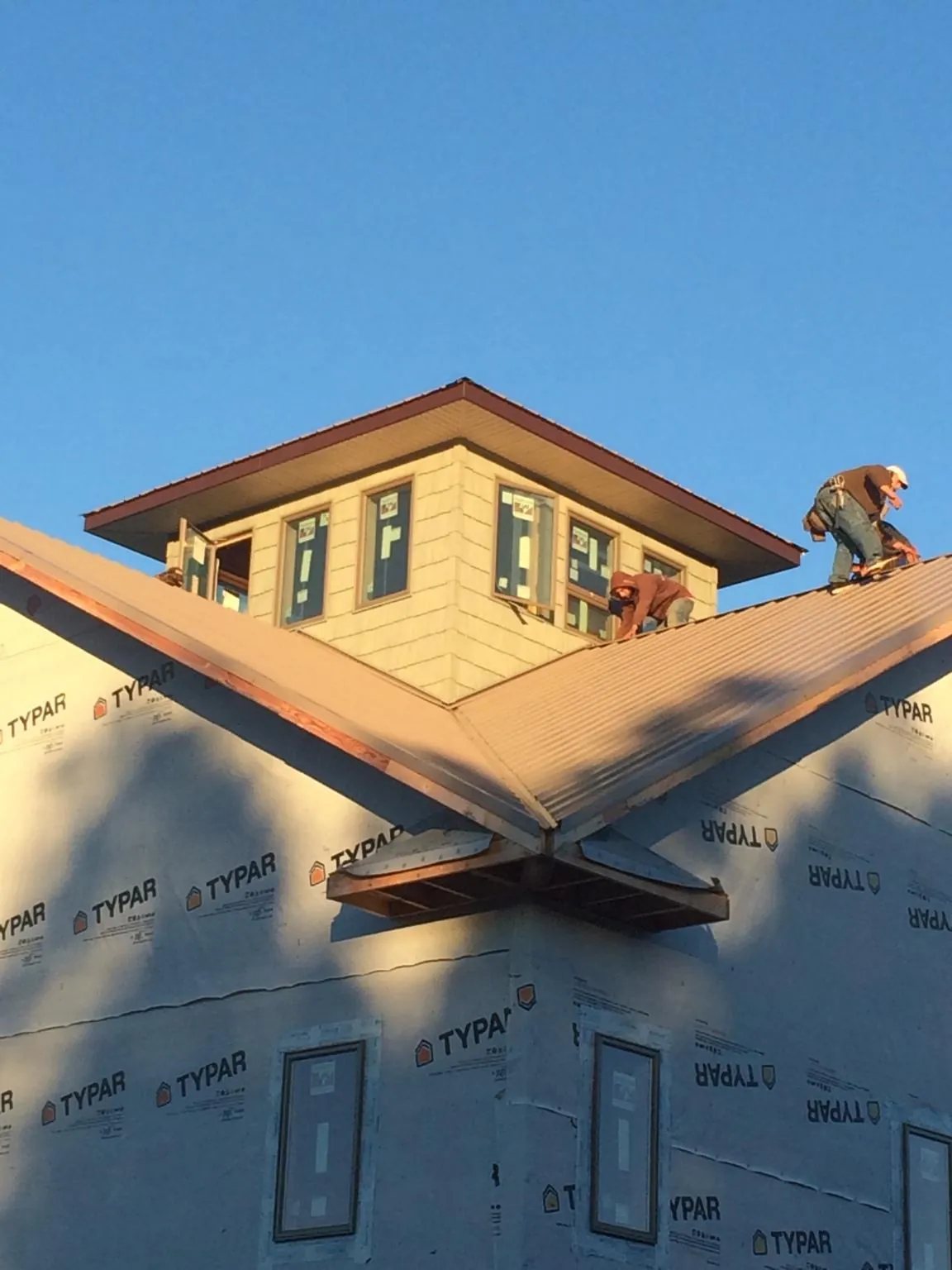 Roofers working around a rooftop cupola on a new metal roof at sunset — Roof Waterproofing in Flora by Roofing Brothers